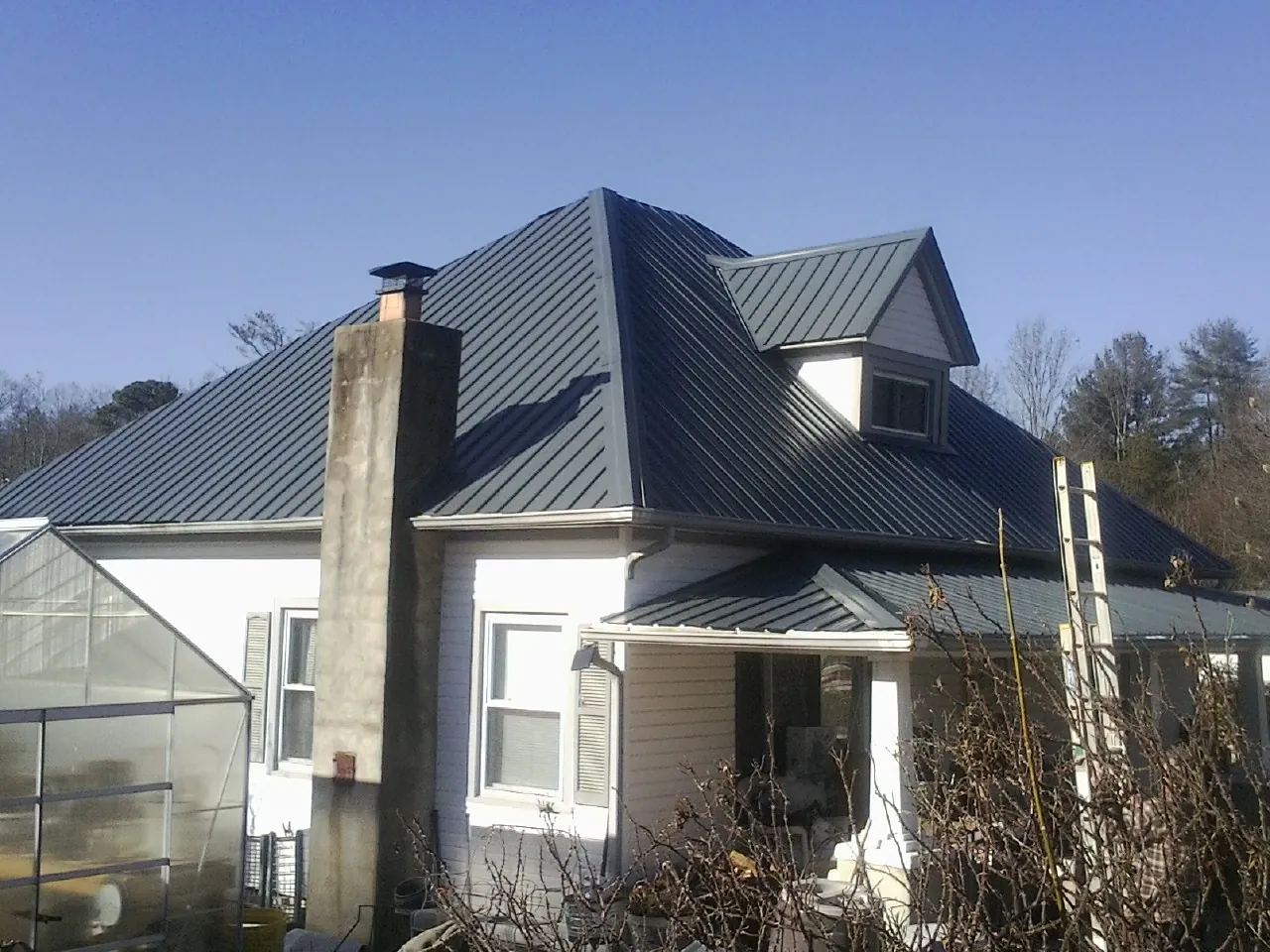 Dark blue standing seam metal roof on a white farmhouse with dormer — Slate & Tile Roof Repair by Roofing Brothers in Lampasas