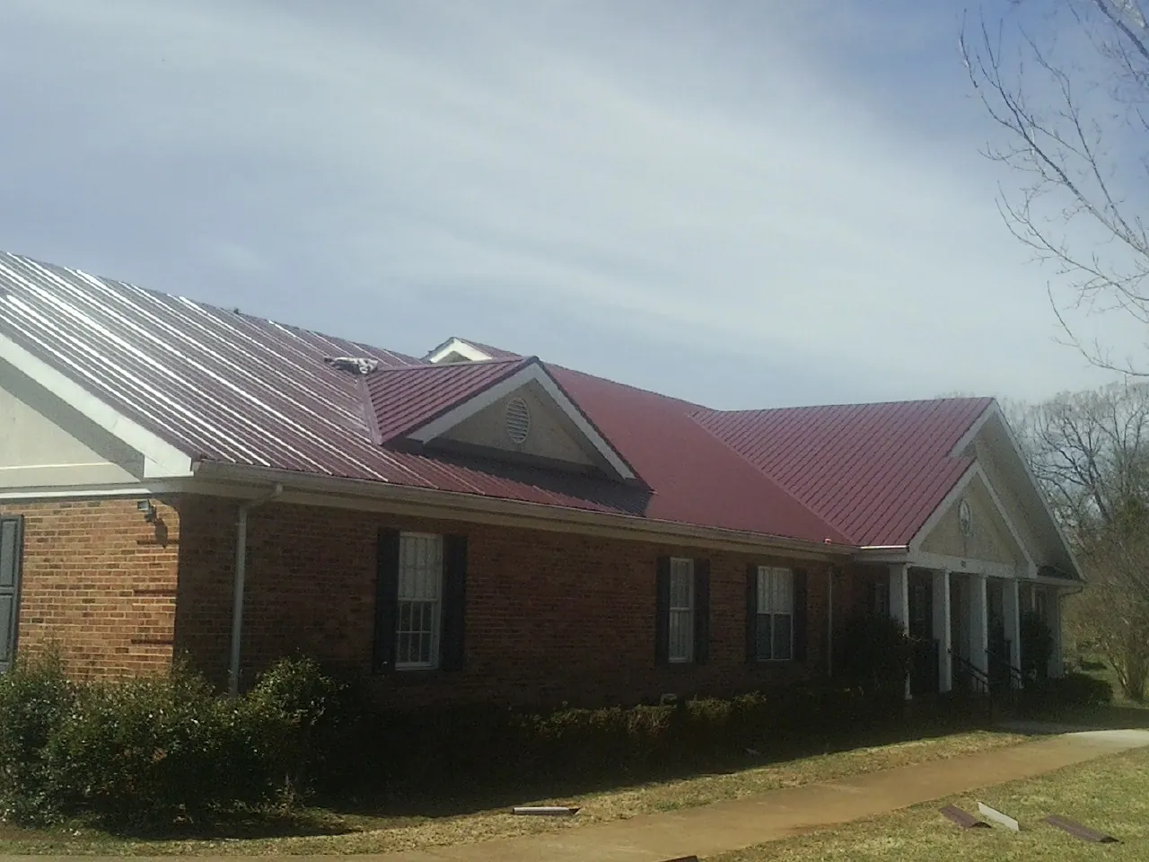 Red metal roof with gabled entries on a long brick building, from a Hail Damage Roof Repair job in Lampasas