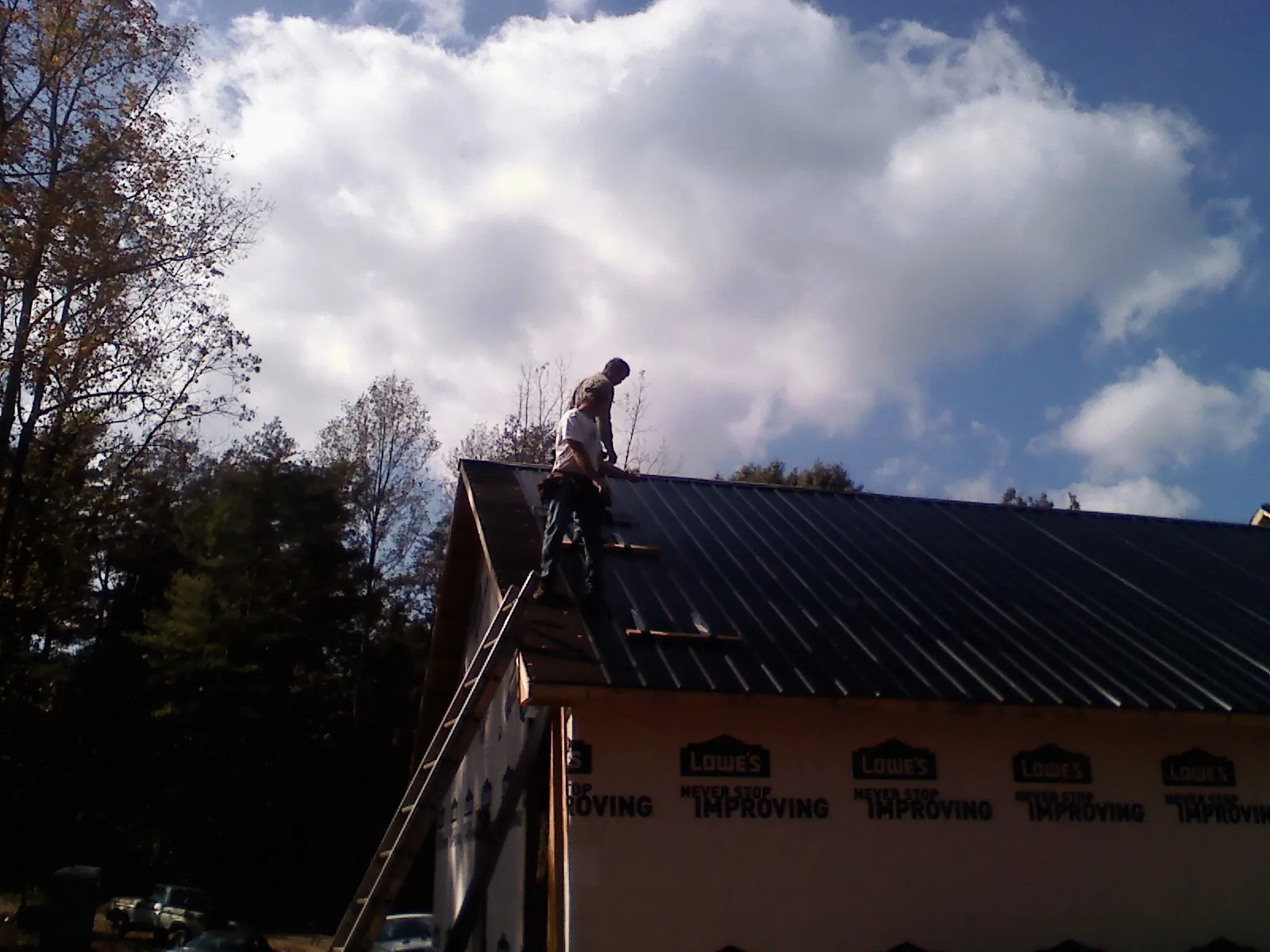 Roofer fastening dark metal panels high against a cloudy sky, from a Roof Inspection job in Lampasas