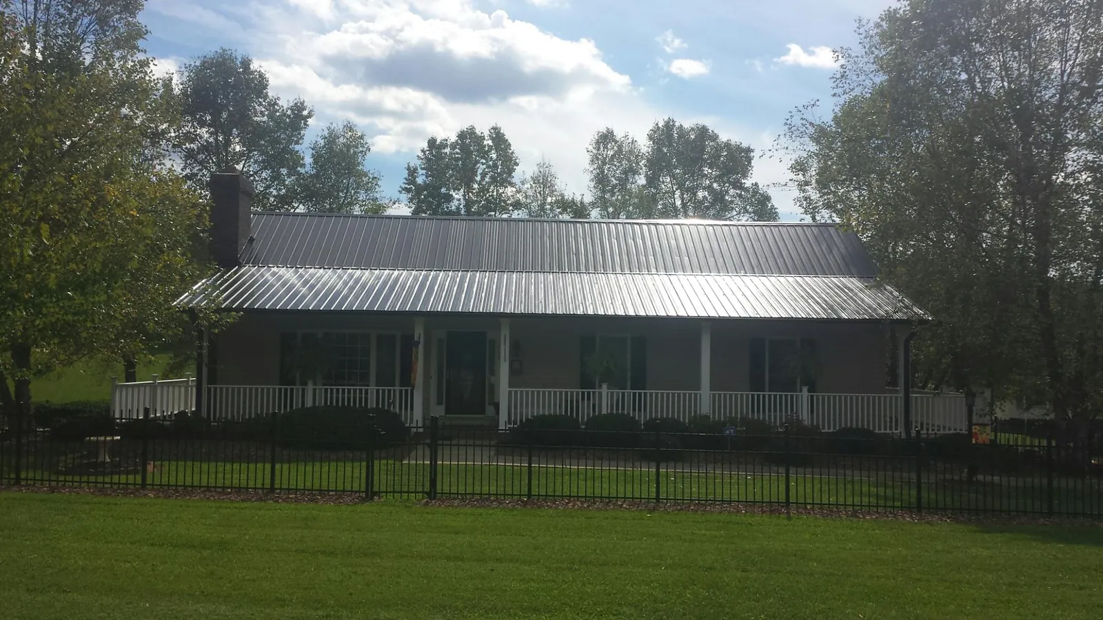Gray metal roof on a brick ranch with a full width front porch — Gutter Guard Installation work by our crew in Lampasas
