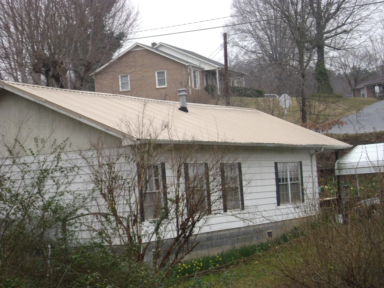 Tan metal roof on a white sided house set into a hillside — Commercial Roofing by Roofing Brothers in Lampasas